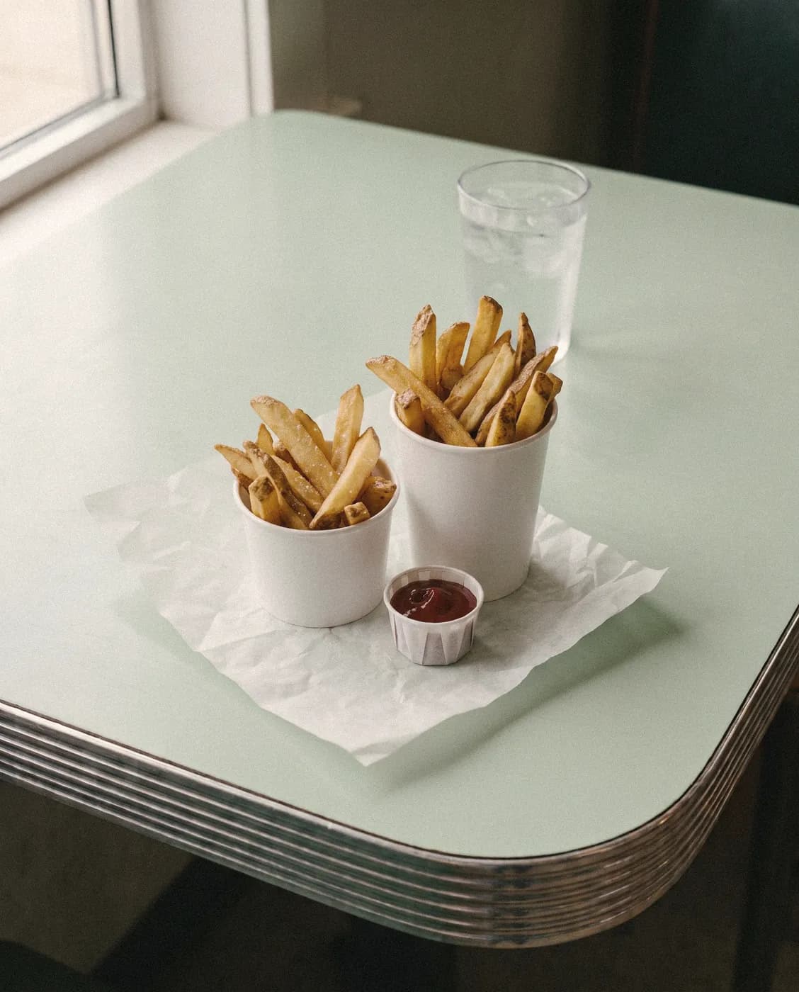 Two paper cups of hand-cut fries with ketchup
