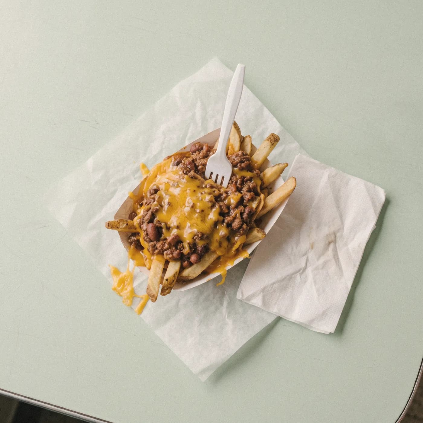 Fries buried under chili and melted cheddar with a plastic fork, seen from above