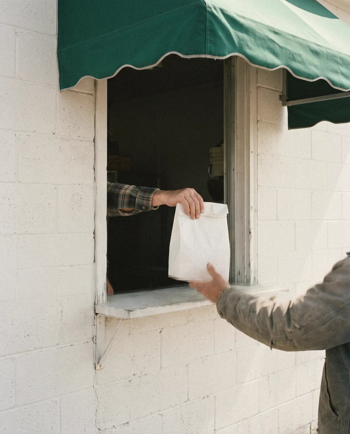 A white paper bag handed out of a serving window under a green awning