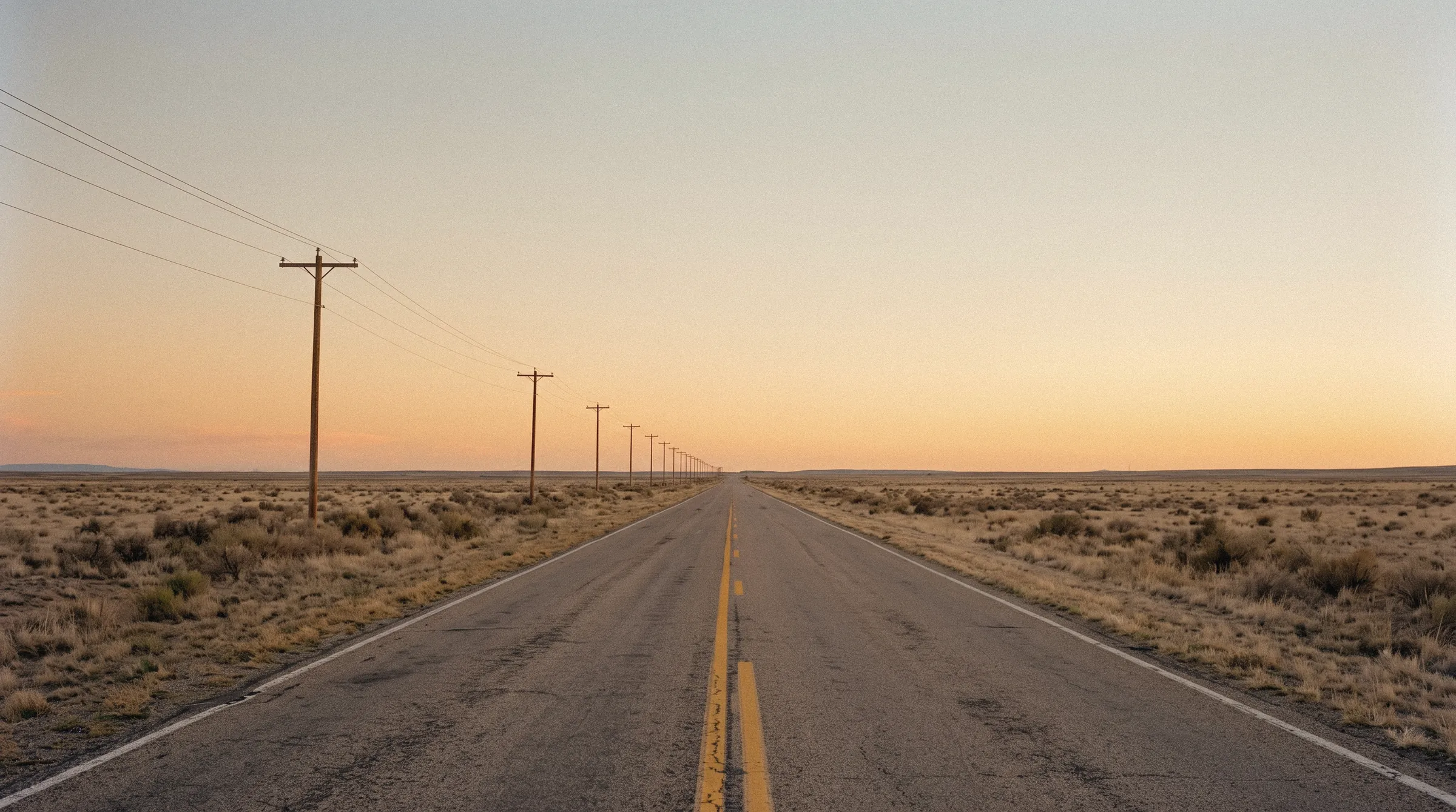 An empty two-lane highway running to the horizon at dusk